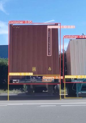 Roadside camera view of two shipping containers on truck chassis with computer vision bounding boxes labeling container, container ID, chassis, and chassis ID with confidence scores.