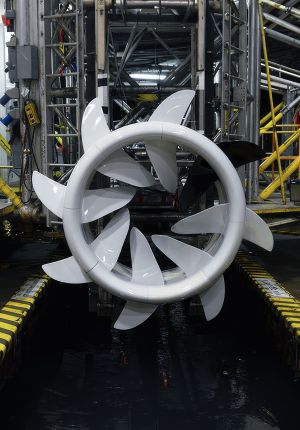 A large white ring-shaped hydrokinetic turbine with curved blades mounted in an industrial test tank surrounded by scaffolding.