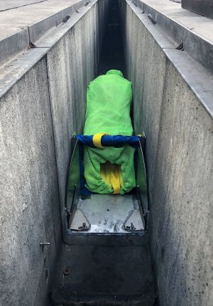 A bright green mesh filter bag mounted in a metal frame inside a concrete storm drain channel, used to capture trash and debris.