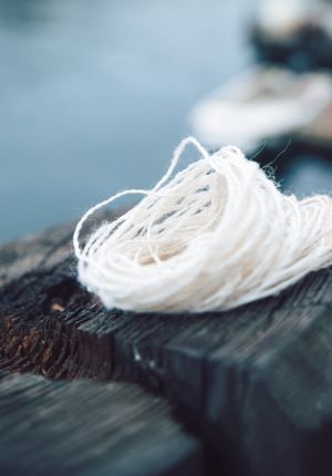 Close-up of a coiled bundle of white natural fiber rope resting on a weathered wooden dock, with blurred water in the background.