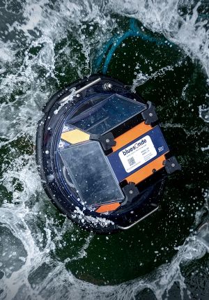 Overhead view of a round orange and navy bluesonde water quality sensor float splashing into dark green water.