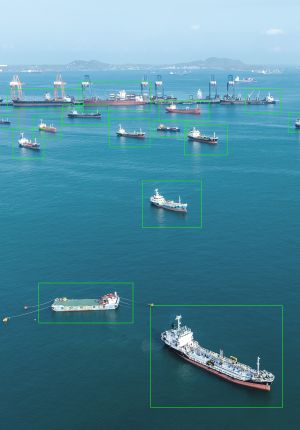 Aerial view of cargo ships and tankers anchored near a port, with green bounding boxes identifying and tracking each vessel.
