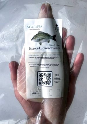 Hand holding a vacuum-sealed fish fillet labeled 'Seatopia — Esteros Lubimar Bream,' with product details and a QR code on the packaging.